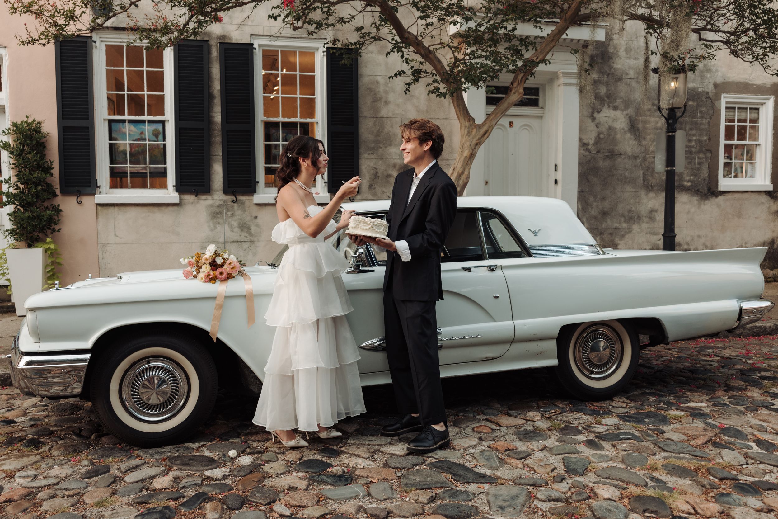 A classic blue vintage Cadillac parked on cobblestone streets is adorned with wedding decorations.