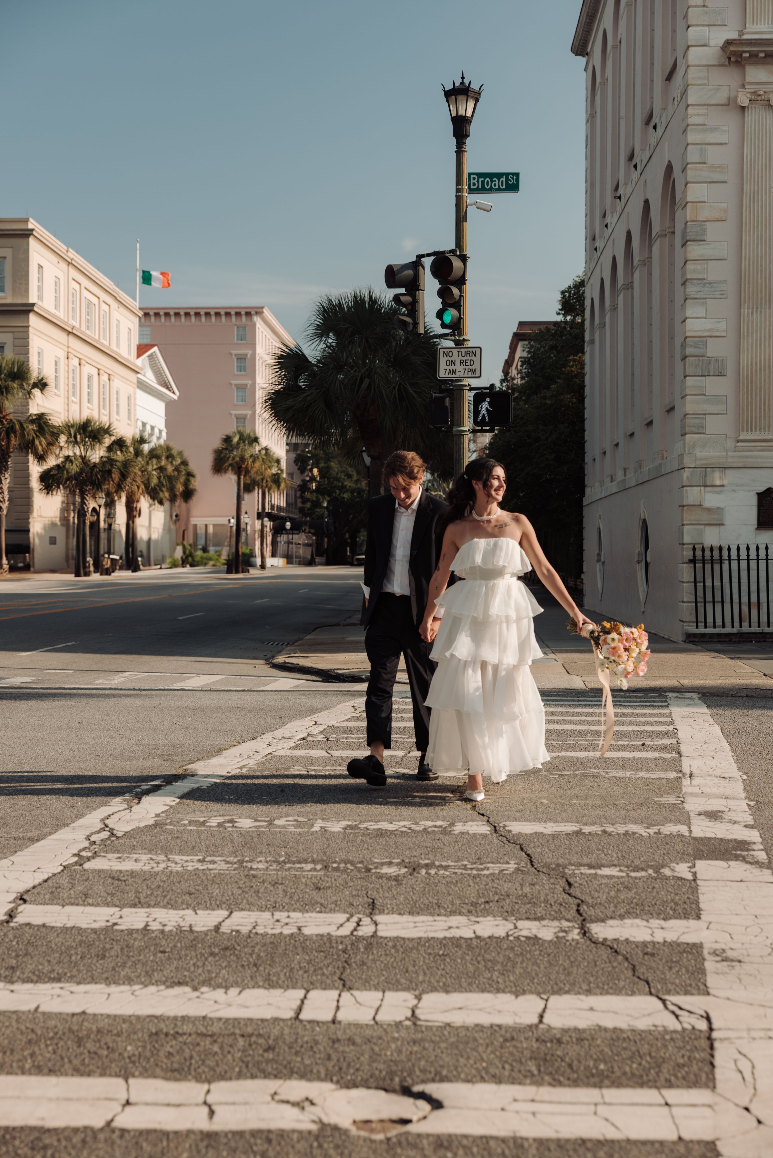 A bridal party walking down a historic street in Charleston with white buildings and palm trees in the background.