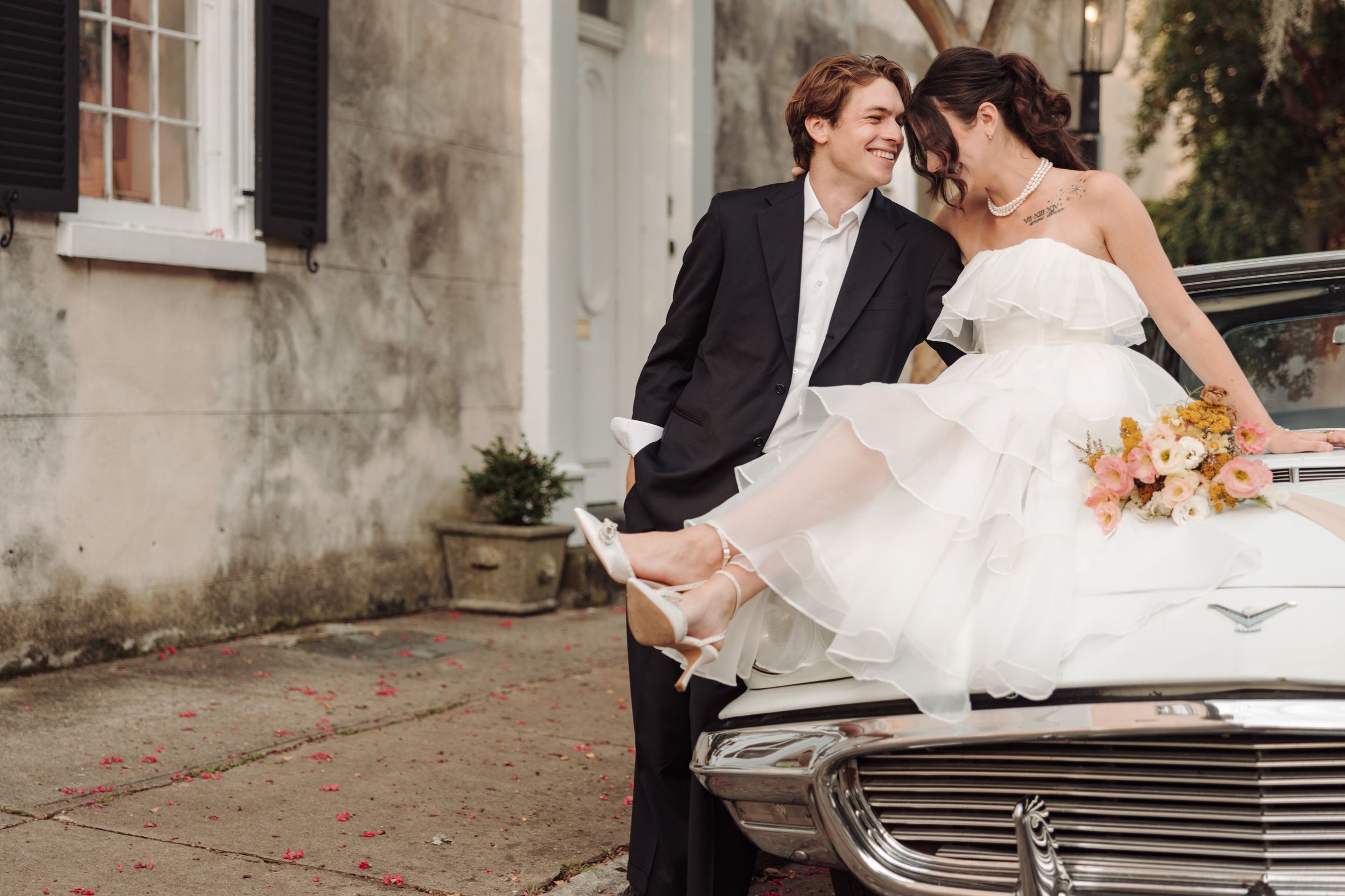 A romantic wedding couple leans against a vintage car while sharing an intimate moment on their special day.