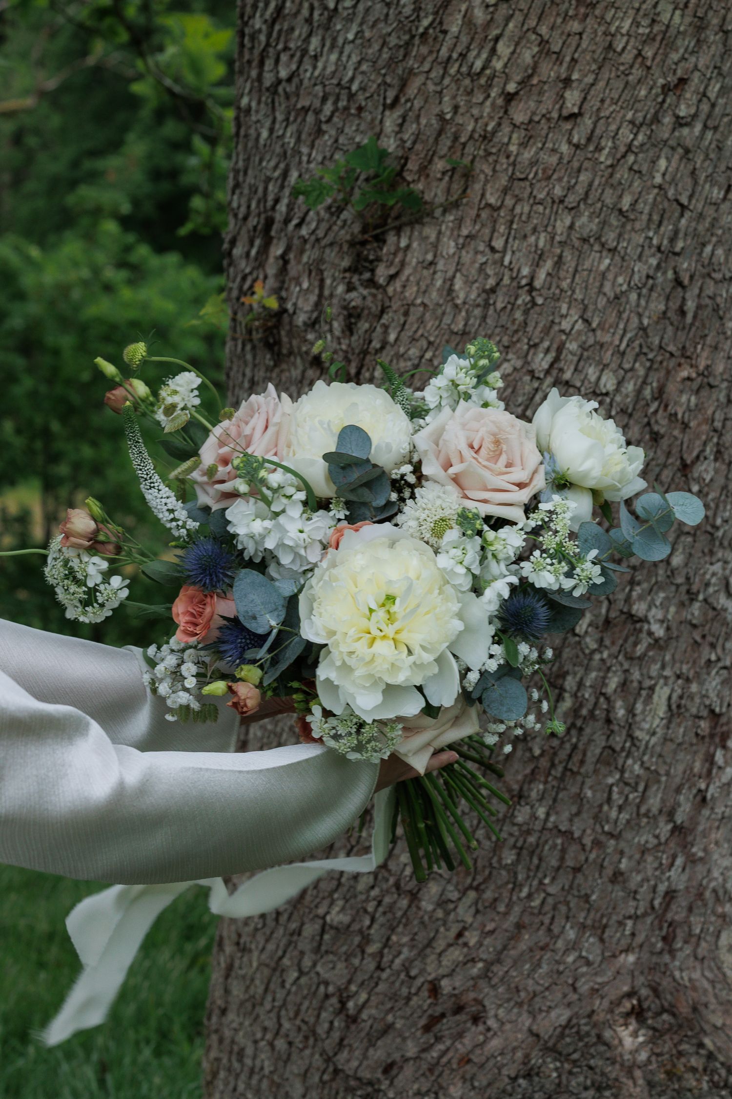 Delicate wedding bouquet with white and blush flowers resting on tree bark.