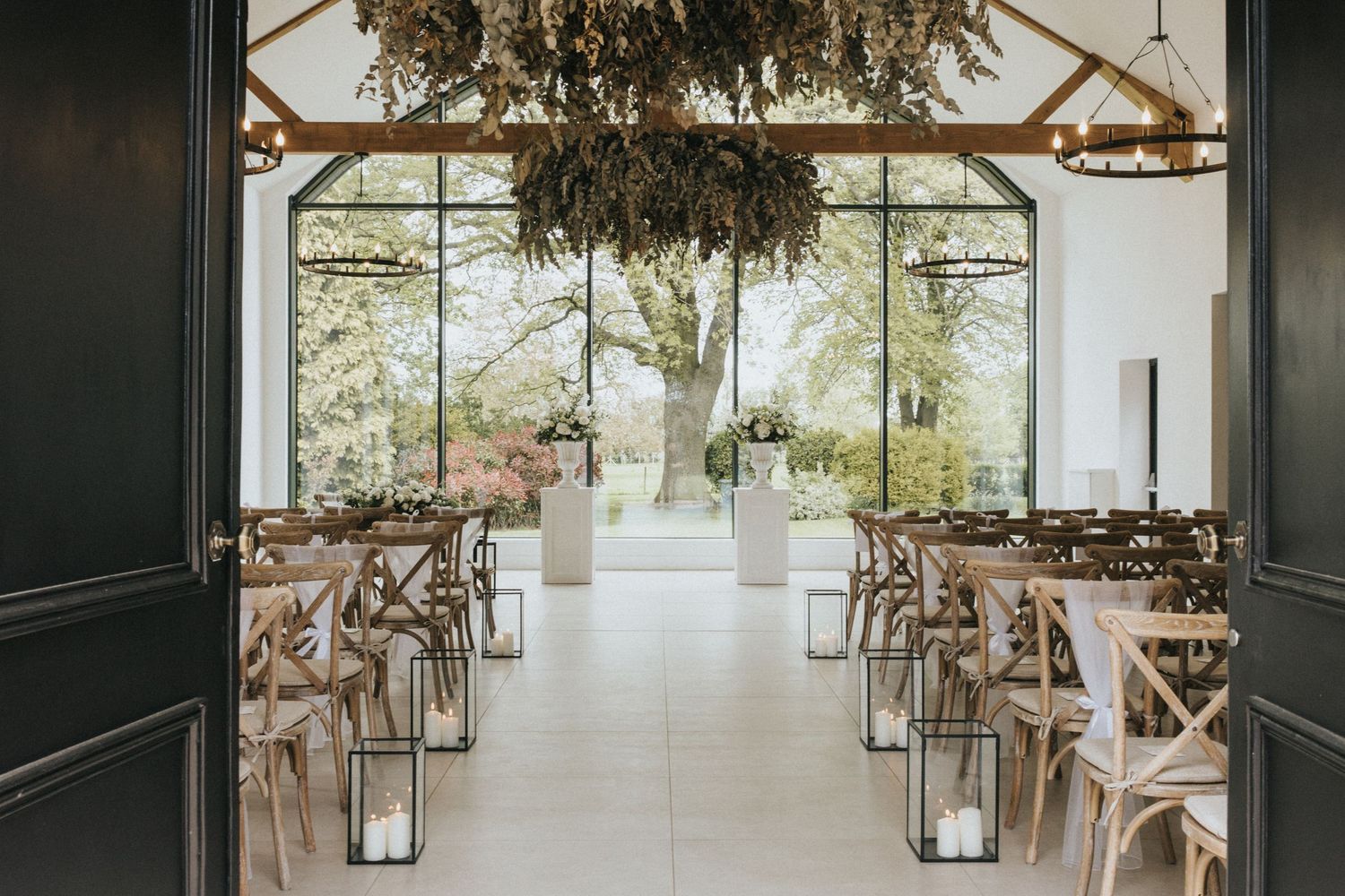 Wedding ceremony taking place in modern white venue with hanging dried floral installation and large windows.