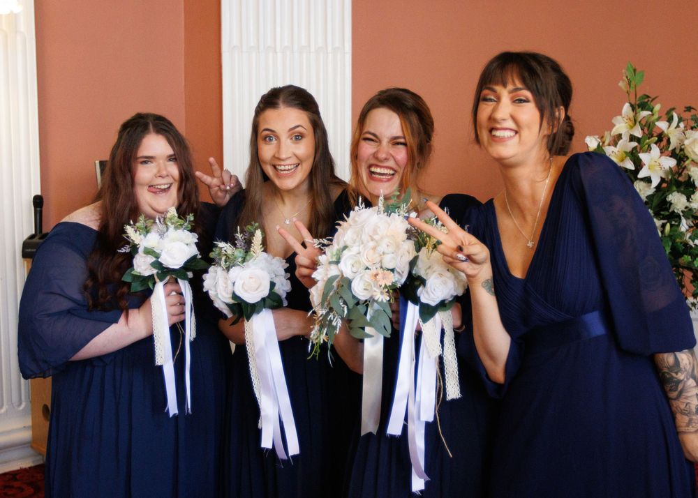 A group of bridesmaids in matching navy blue dresses holding white and blush floral bouquets with ribbons.
