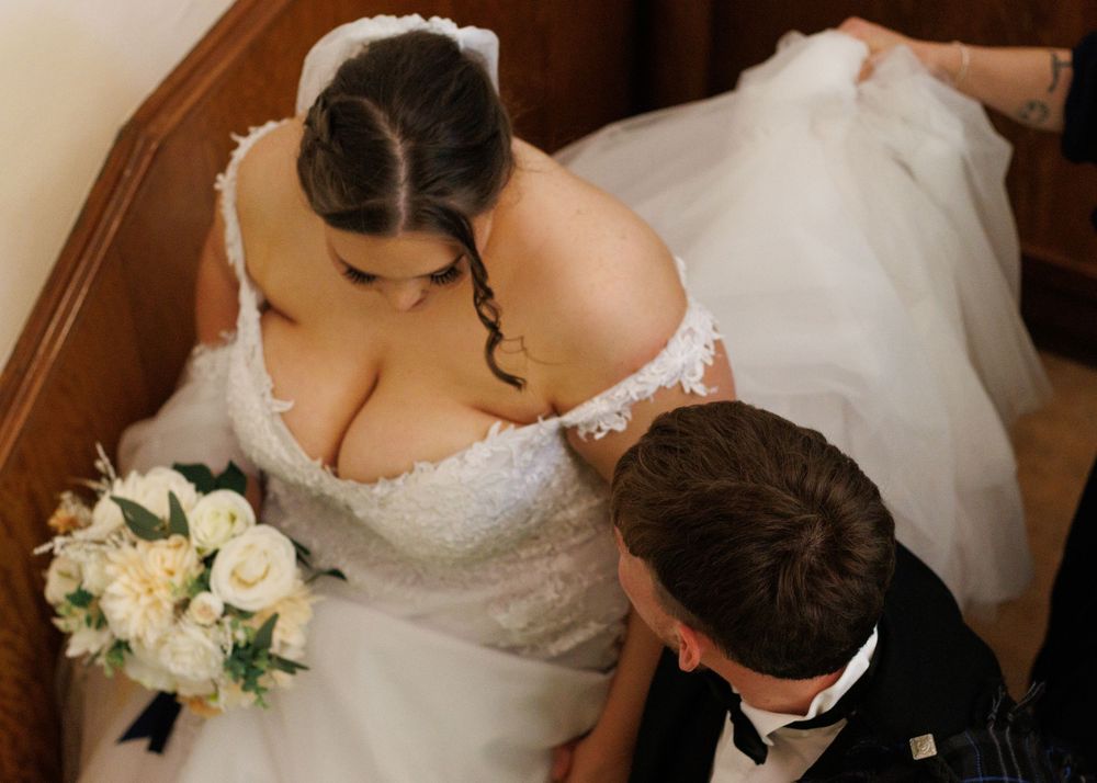 A bride holds white roses in her lace wedding dress while sharing an intimate moment from above.