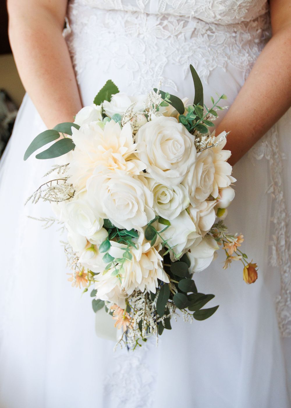 Elegant white and cream wedding bouquet with roses, dahlias and eucalyptus greenery against lace dress.