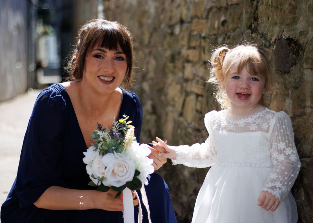 A pair wearing wedding attire share a joyful moment together against a stone wall background.