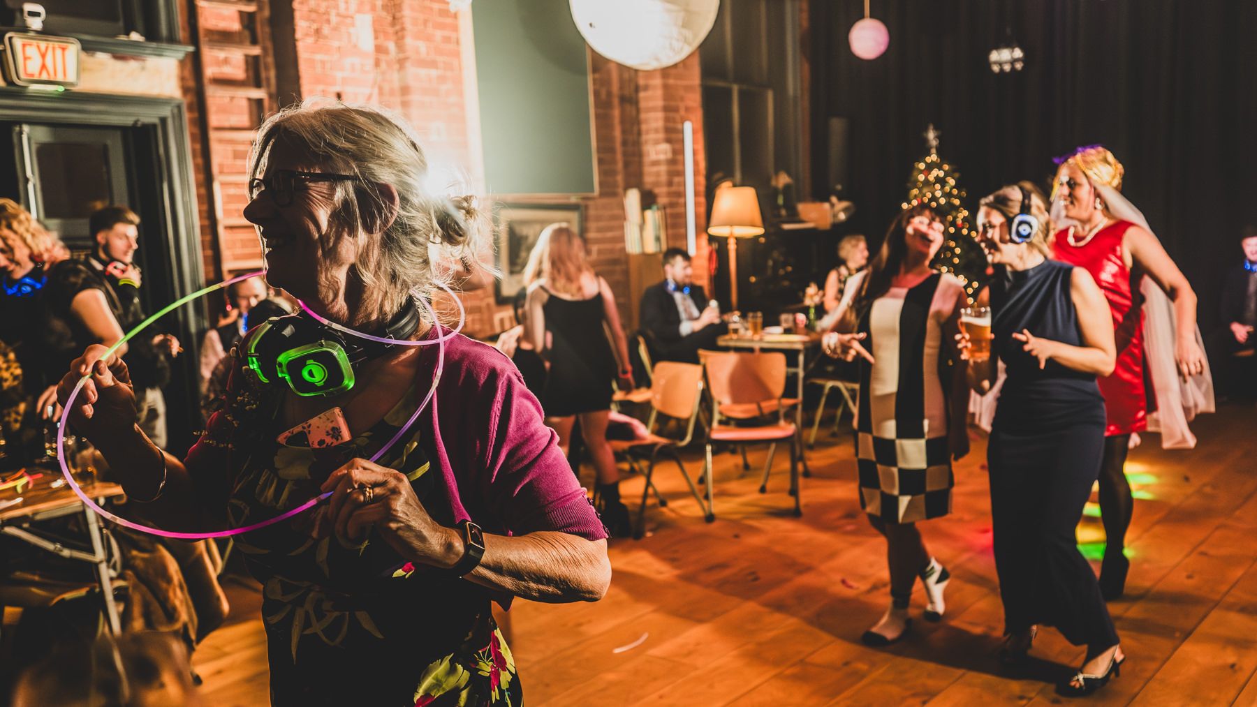 People dancing and enjoying live music in a warm, brick-walled venue with hanging lights and festive decorations.