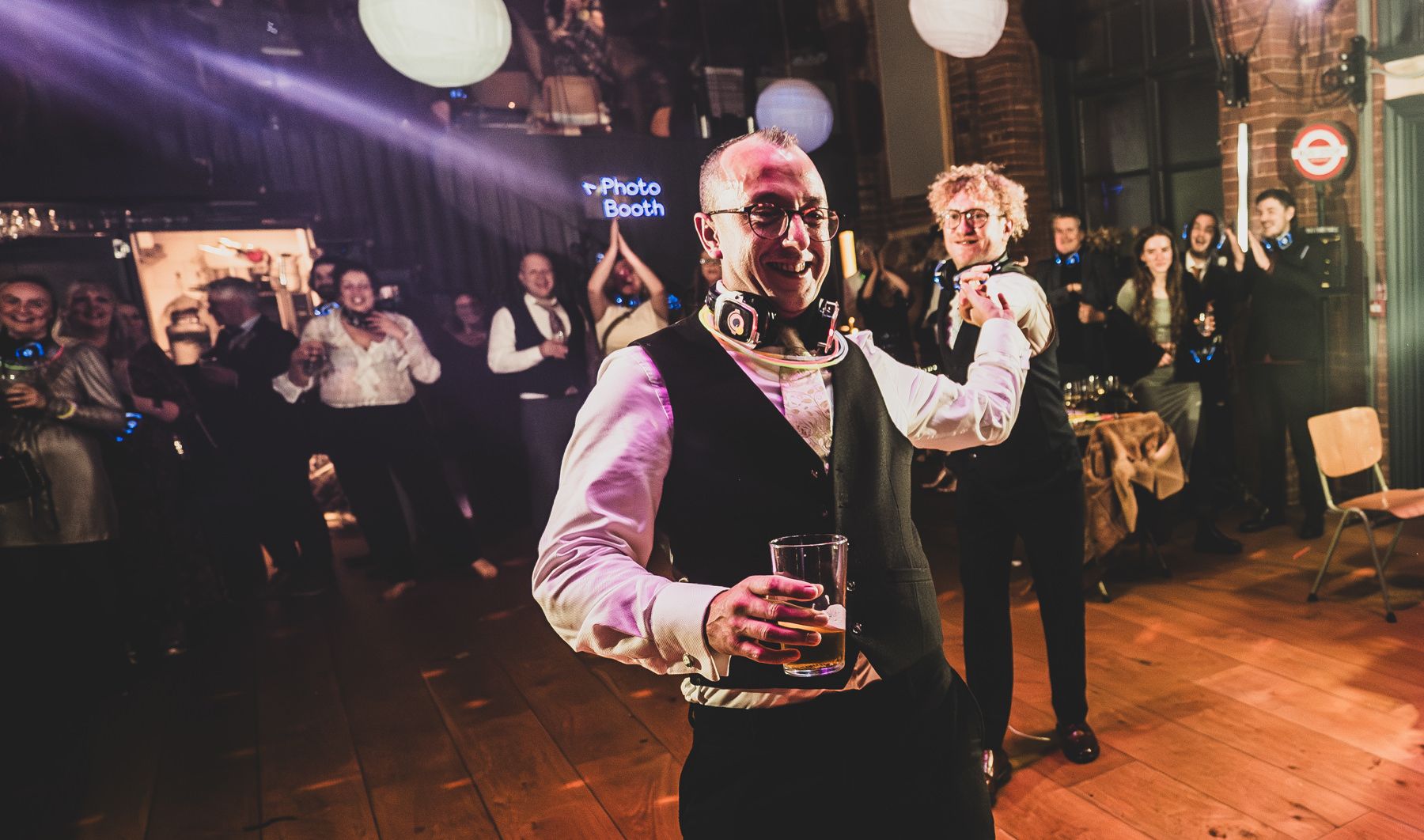 Wedding party dances and celebrates on a dimly lit dance floor decorated with hanging paper lanterns.