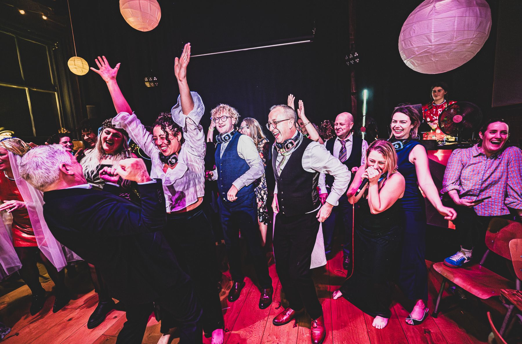 Large group of party-goers dancing and enjoying themselves under pink paper lanterns at a nighttime event.