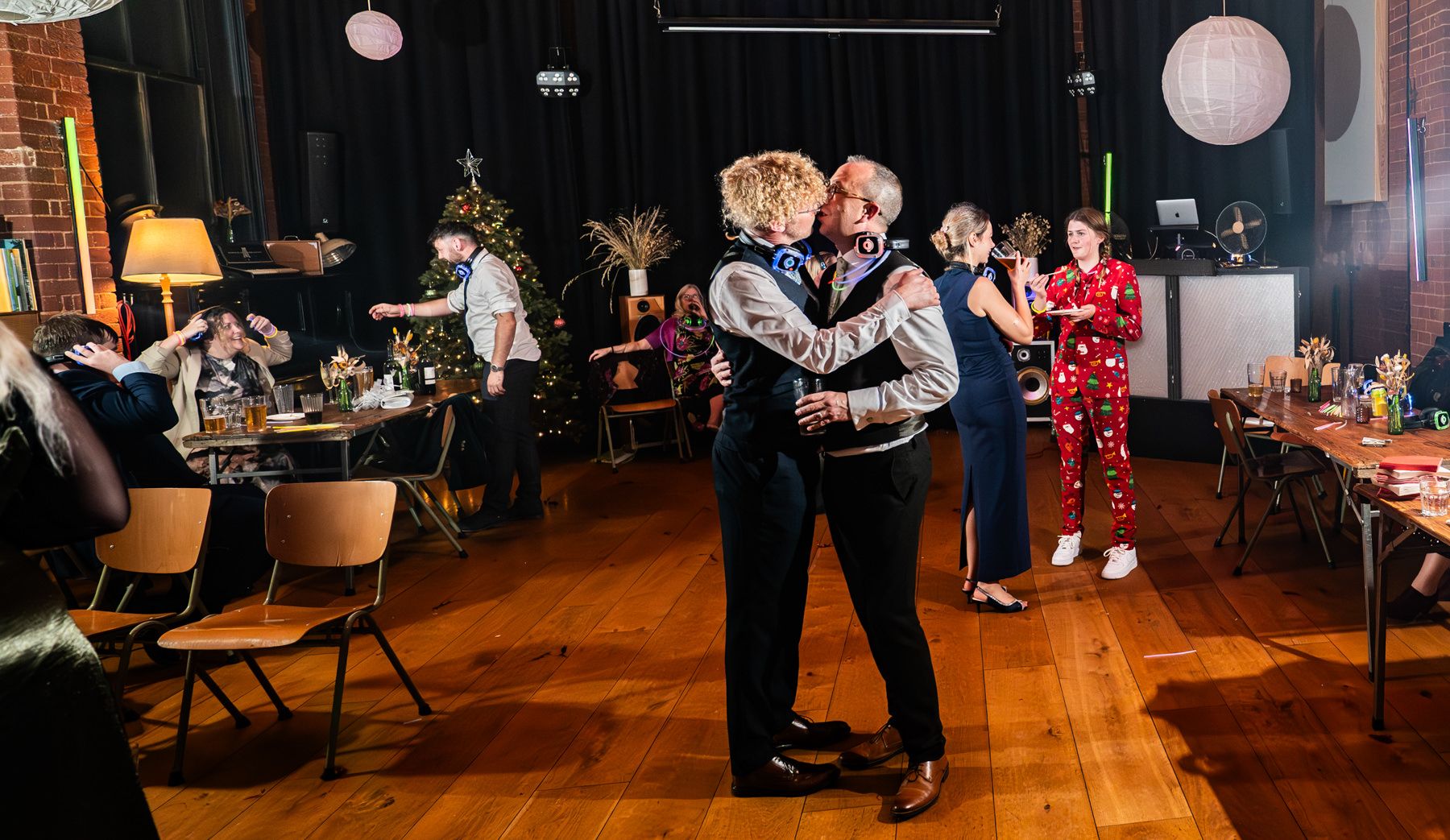 Couples dance together during an indoor party with paper lanterns and warm lighting on a wooden floor.