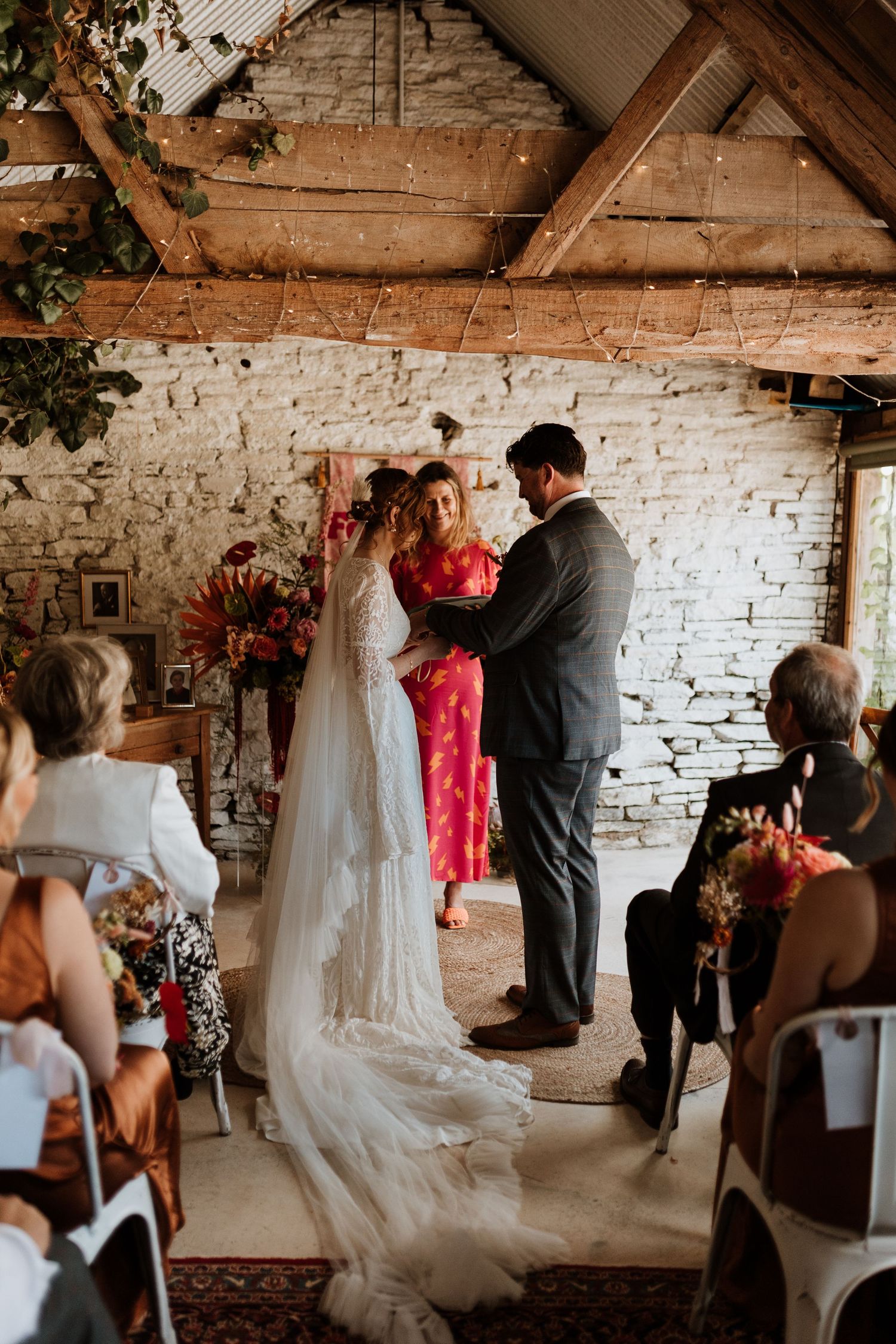 A wedding ceremony takes place in a rustic venue with exposed brick walls and wooden beams overhead.