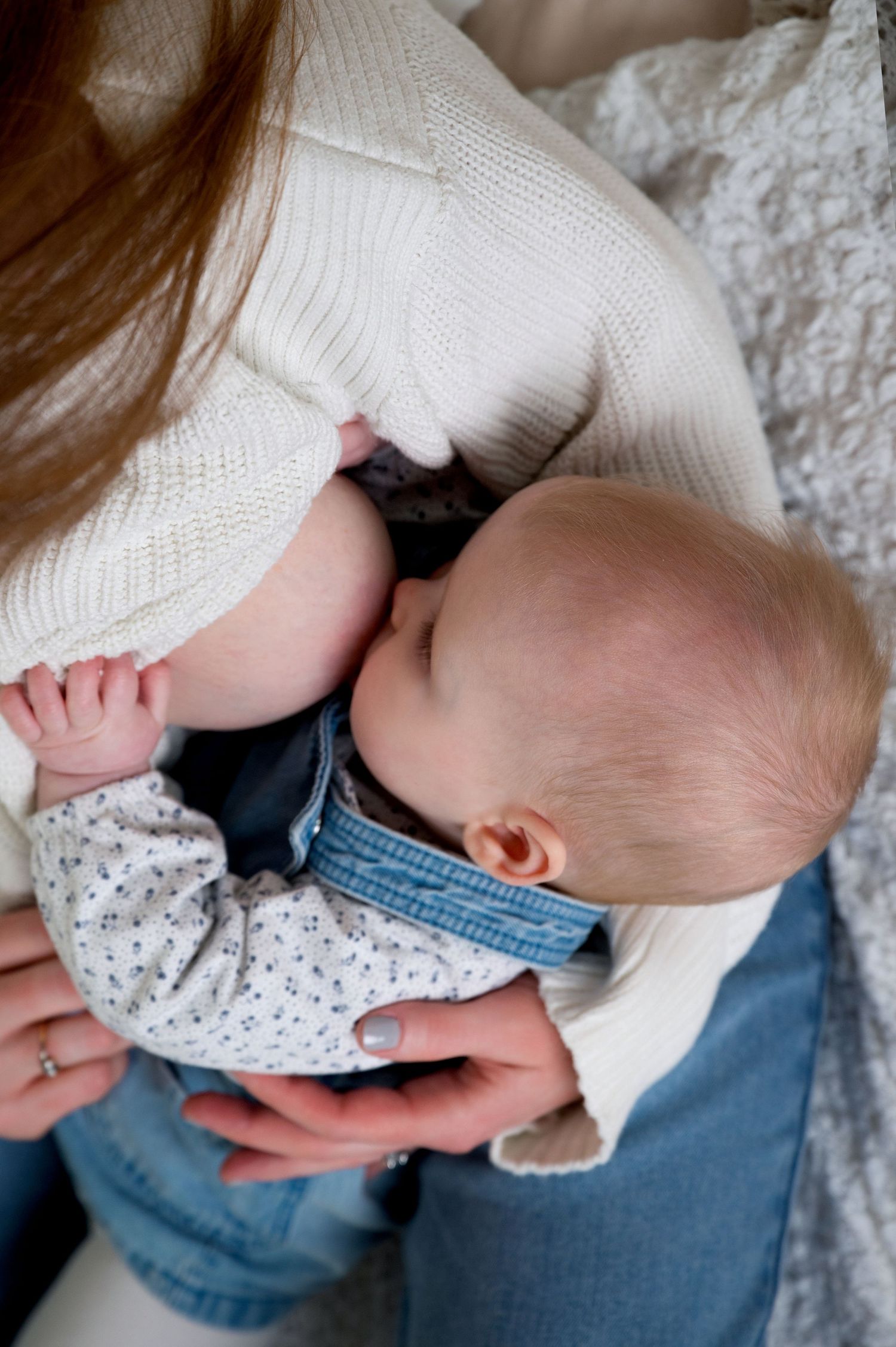 Four close-up shots of a small infant being cradled in someone's arms while wearing a white sweater and blue jeans.