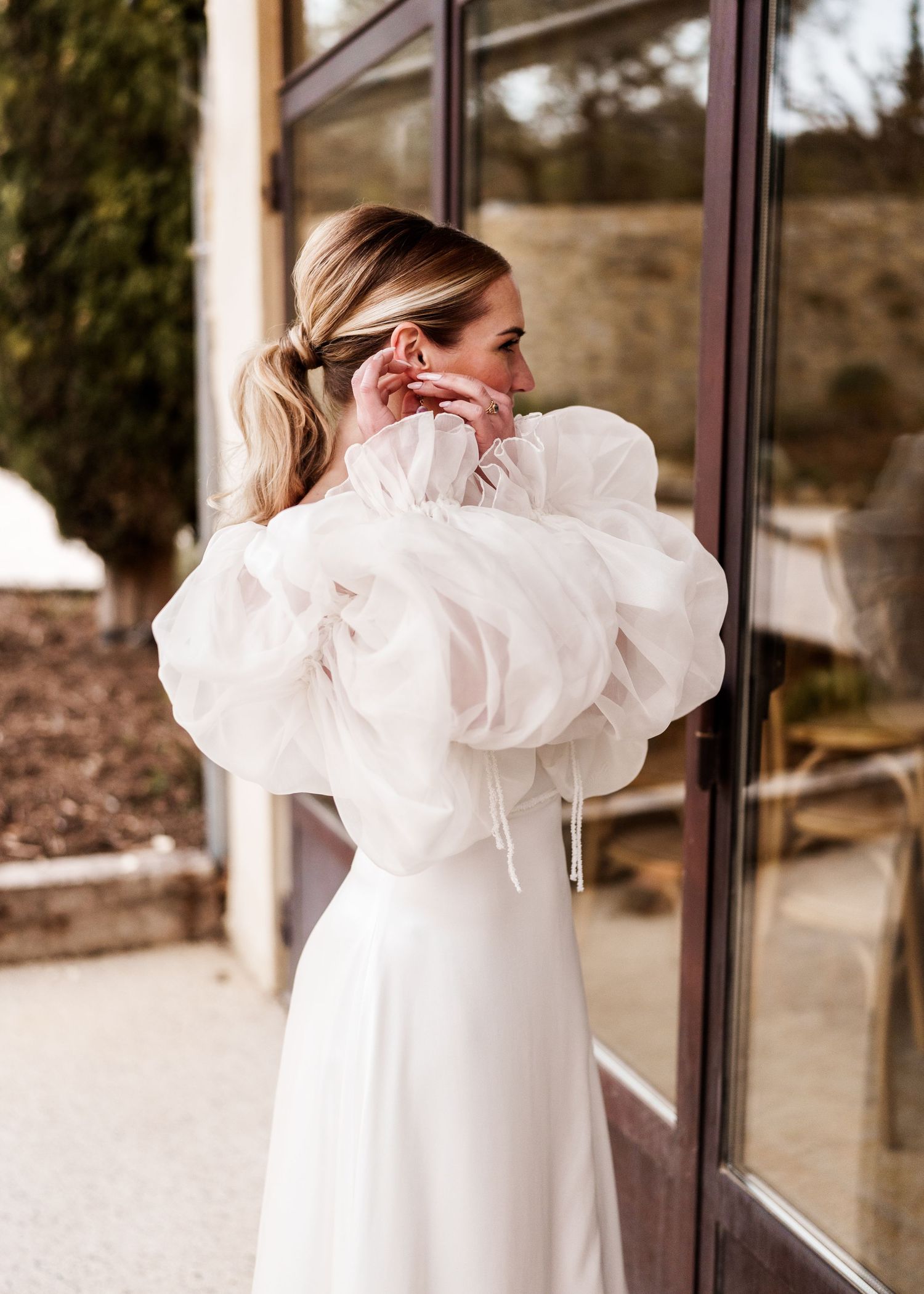 A bride in a white dress with dramatic puff sleeves looking over her shoulder.