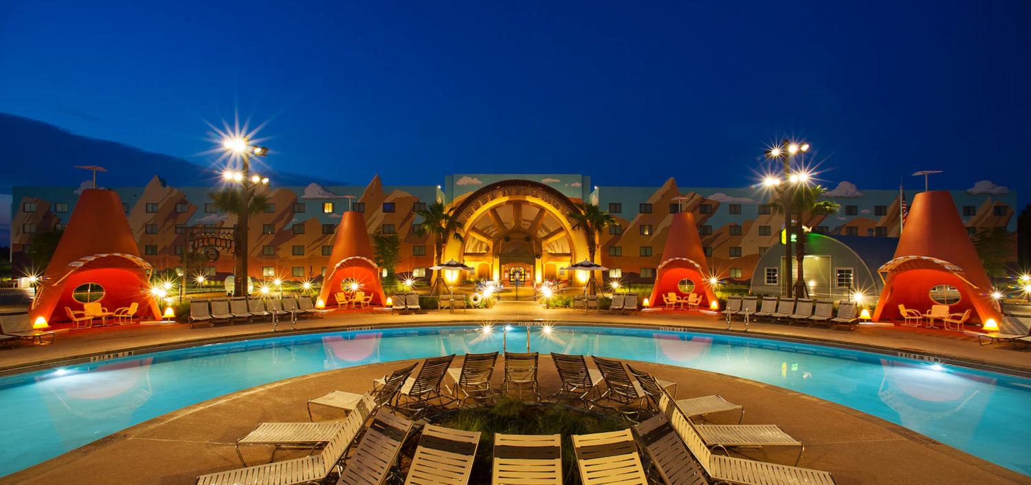 Illuminated pool area at dusk with red cone-shaped structures and palm trees at Disney resort.