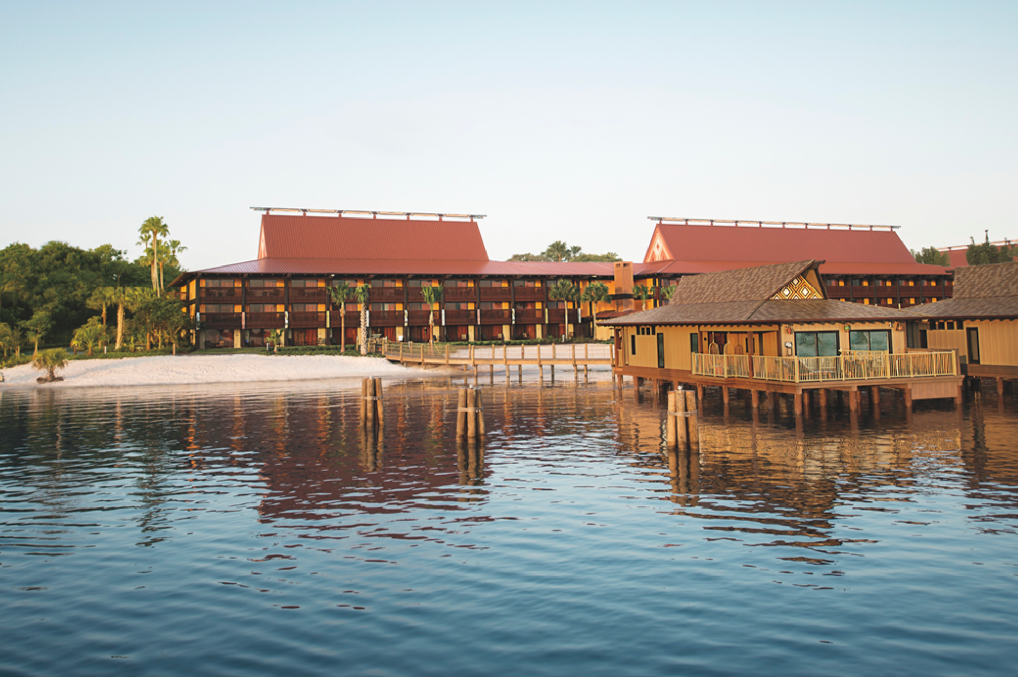 Polynesian-style buildings with red roofs built over water at a Disney resort.