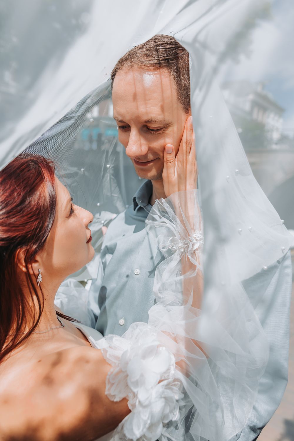 A romantic wedding couple shares an intimate moment under a flowing white veil.