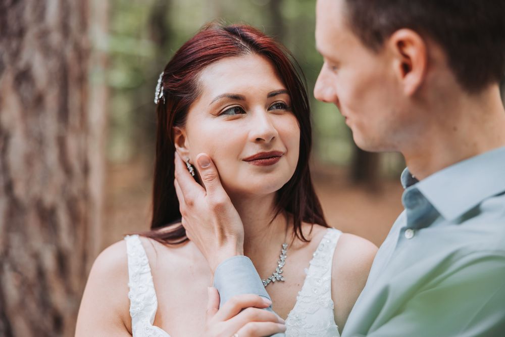 A couple shares an intimate moment in a forest setting wearing elegant wedding attire.