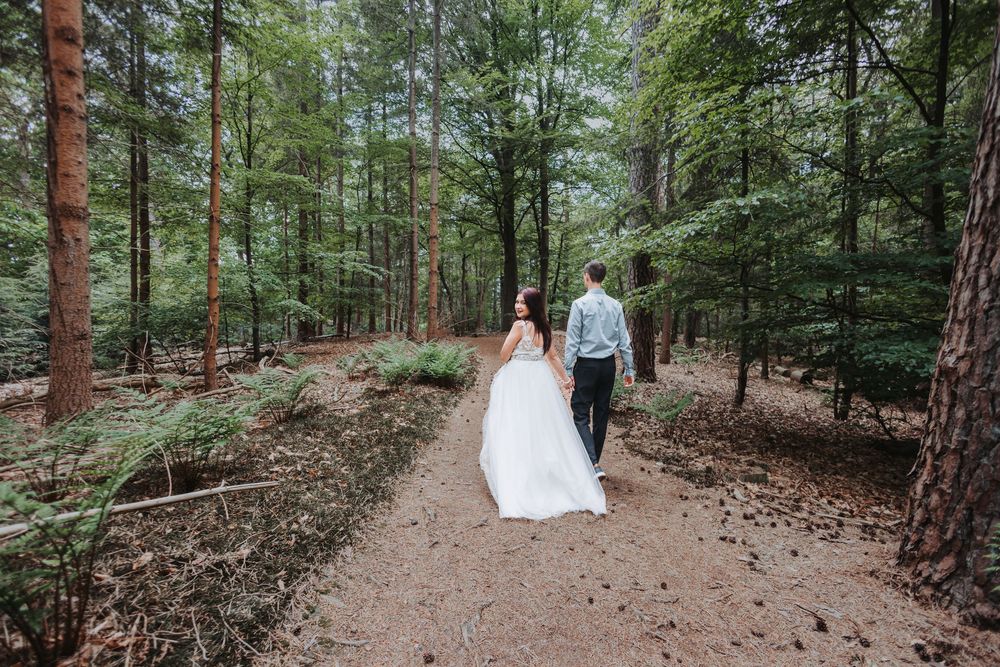 A couple walks through a serene pine forest path during a wedding photoshoot.