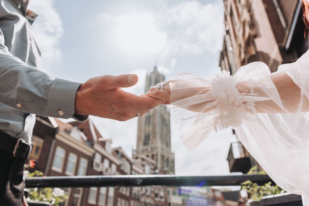 A bride and holding hands with the Domtoren in Utrecht in the background.