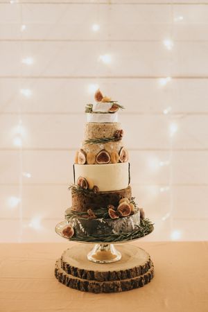 Two-tier woodland-themed wedding cake with forest elements and greenery on a wooden slice stand.
