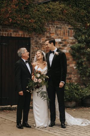 Lively candid wedding party moment shared outdoors against a rustic brick wall with green ivy.