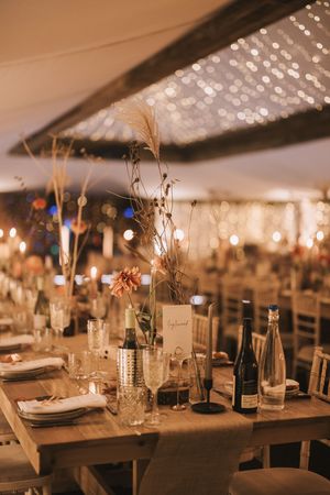 Elegant wedding reception tables set under white draped ceiling with twinkling lights and rustic decor details.