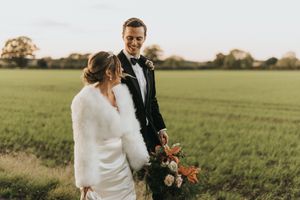 Wedding couple walks through a sunny green field during golden hour celebration at their countryside ceremony.