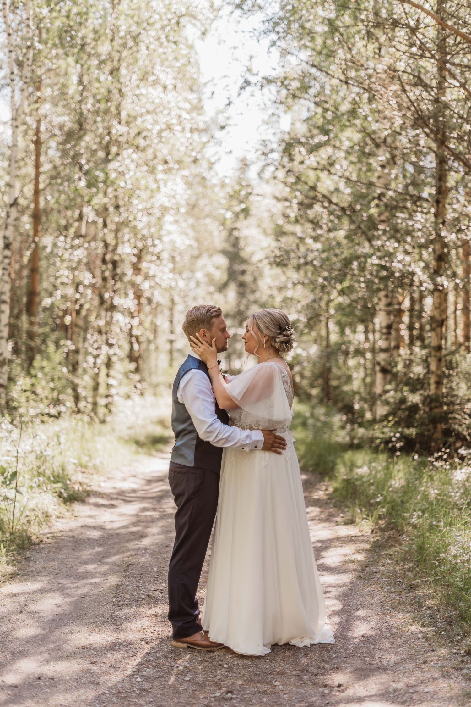 Two small children in formal attire share a sweet moment on a sunlit forest path.