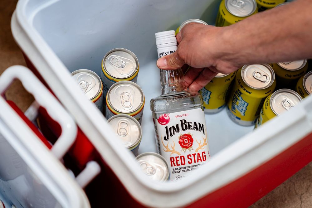 Various cans of beer and liquor bottles chilling in a white cooler filled with ice.