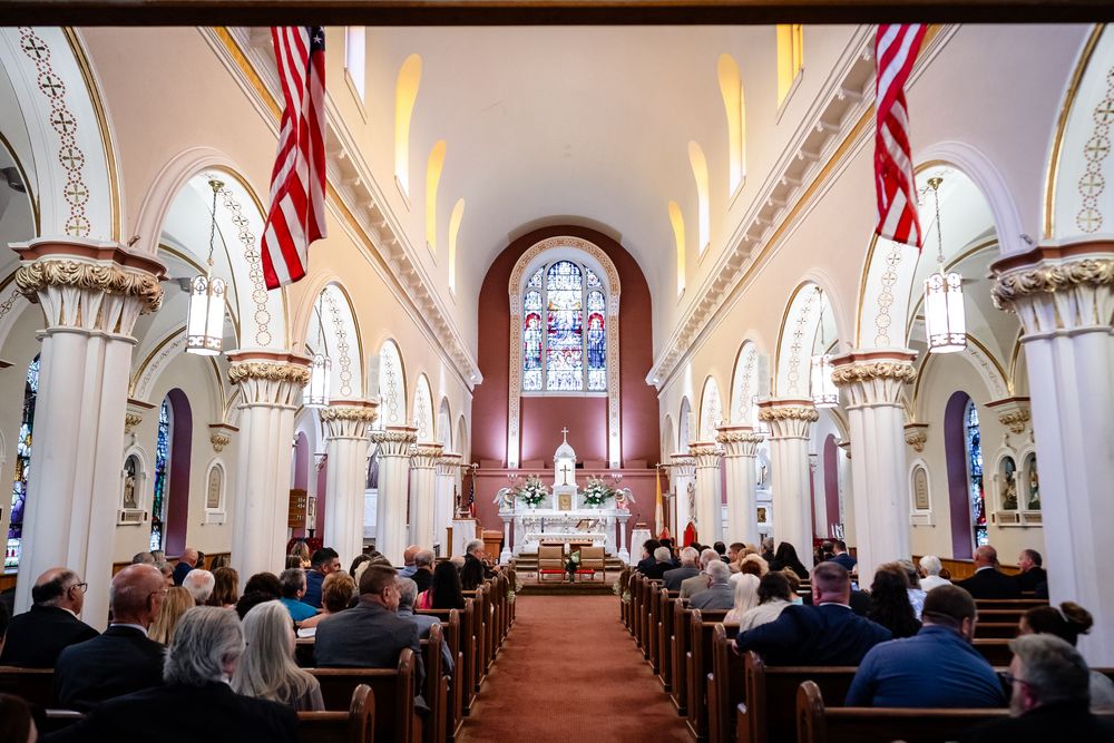 Panoramic view of traditional church interior with arched ceilings and American flags during wedding ceremony.