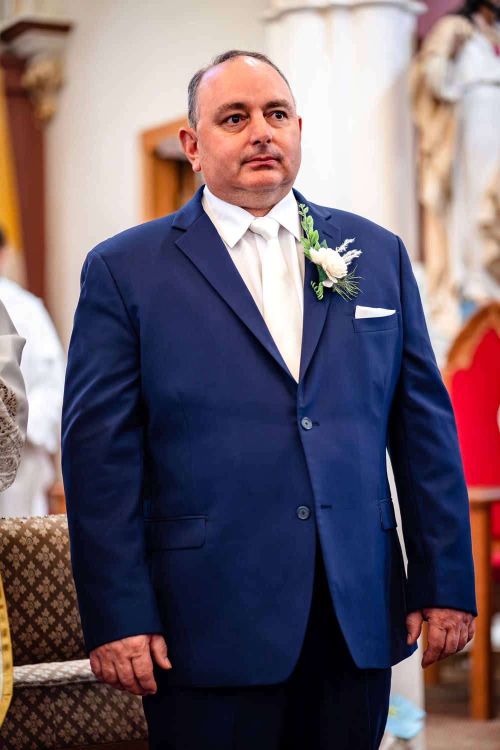 Groomsmen in navy blue suits with white boutonnieres stand in church during wedding ceremony.