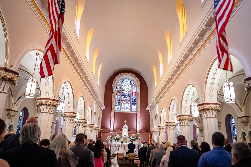 Interior of a Catholic church with ornate architecture and American flags during a wedding ceremony.