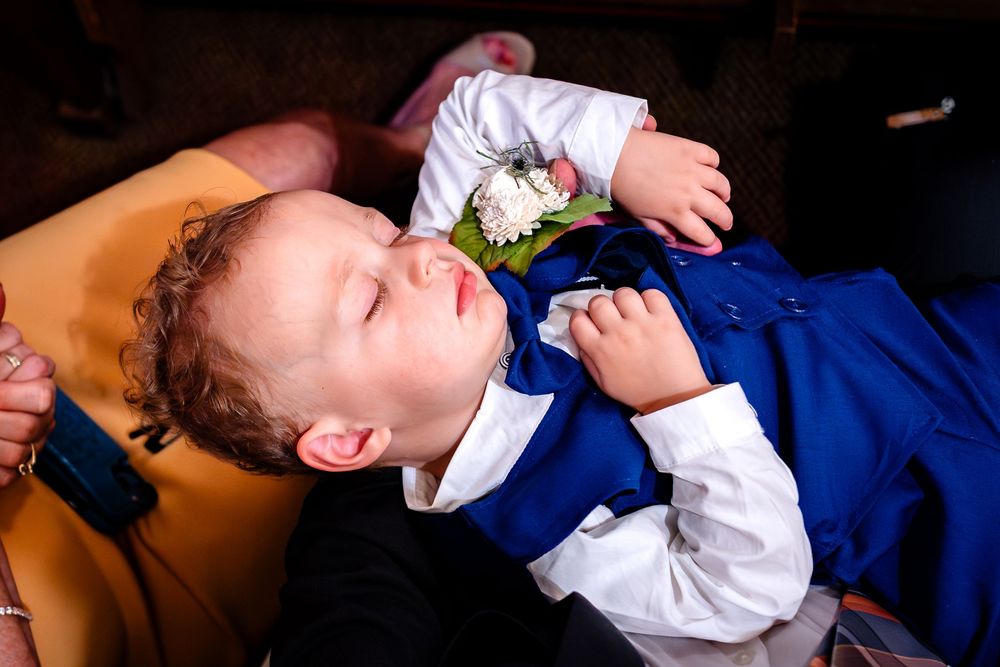 Young ring bearer in blue suit resting during wedding ceremony.
