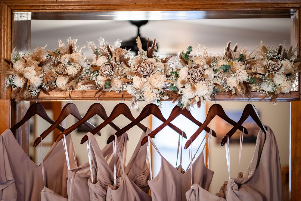 Row of pink and white bridesmaid dresses hanging on decorative hangers beneath floral arrangements.