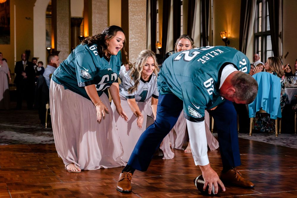 Wedding guests in teal jerseys dancing energetically at reception celebration.