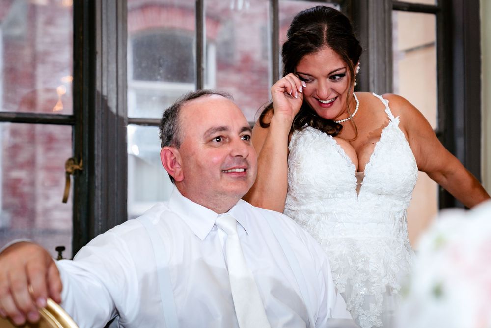 Wedding party members laugh and embrace during an emotional reception moment.