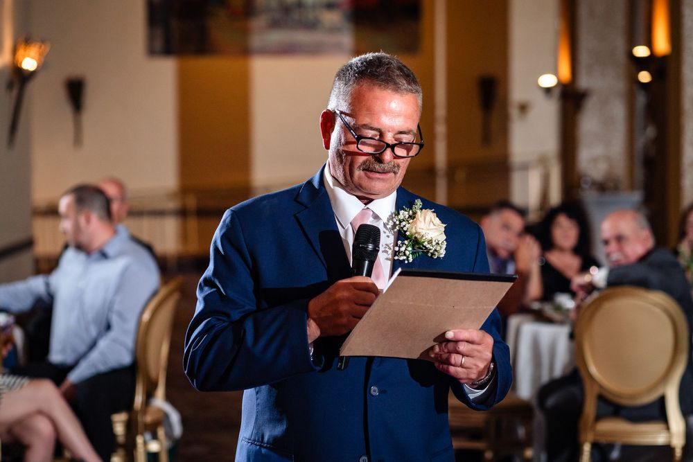 Man in navy suit gives heartfelt speech at wedding reception.