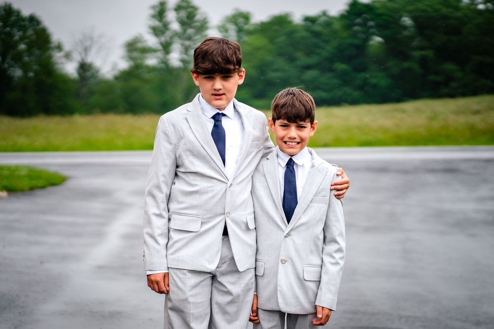 Wedding party walking together on wet pavement in white formal attire.