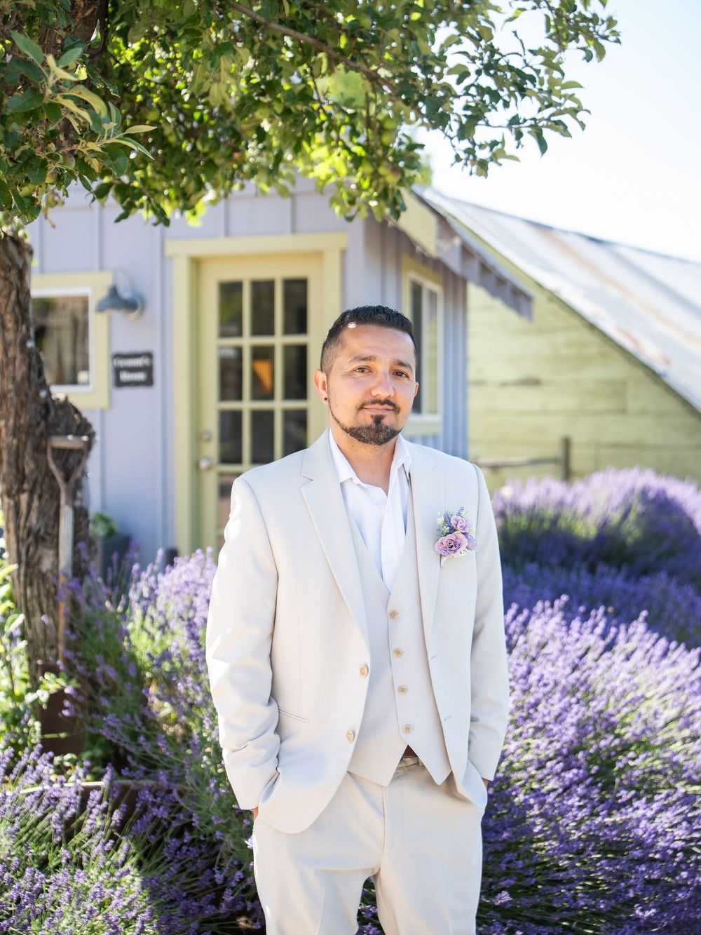 A stylish cream-colored suit worn against a backdrop of blooming lavender and a rustic white building.