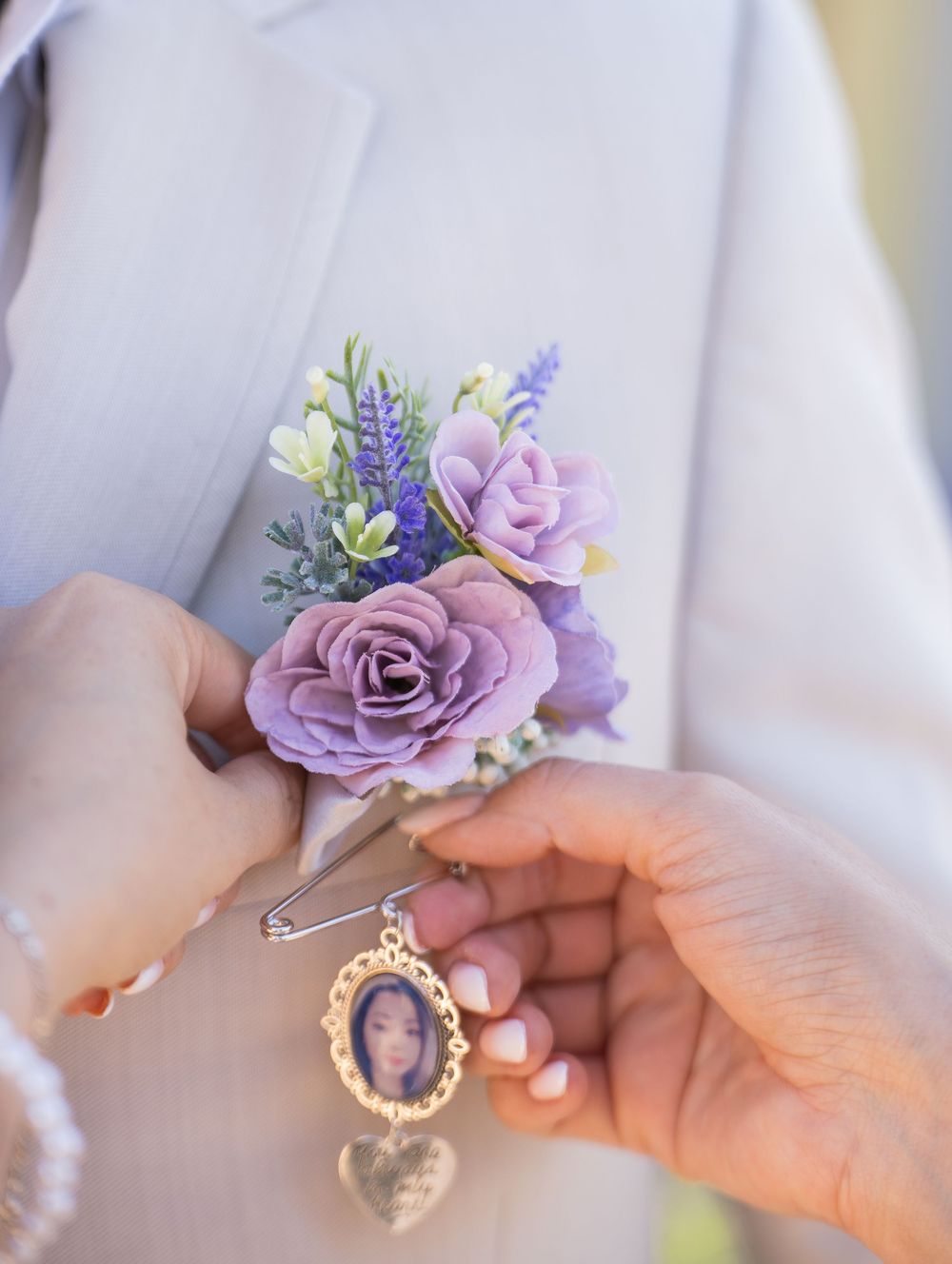 Wedding bouquet with purple roses and lavender sprigs next to hands holding a vintage locket pendant.