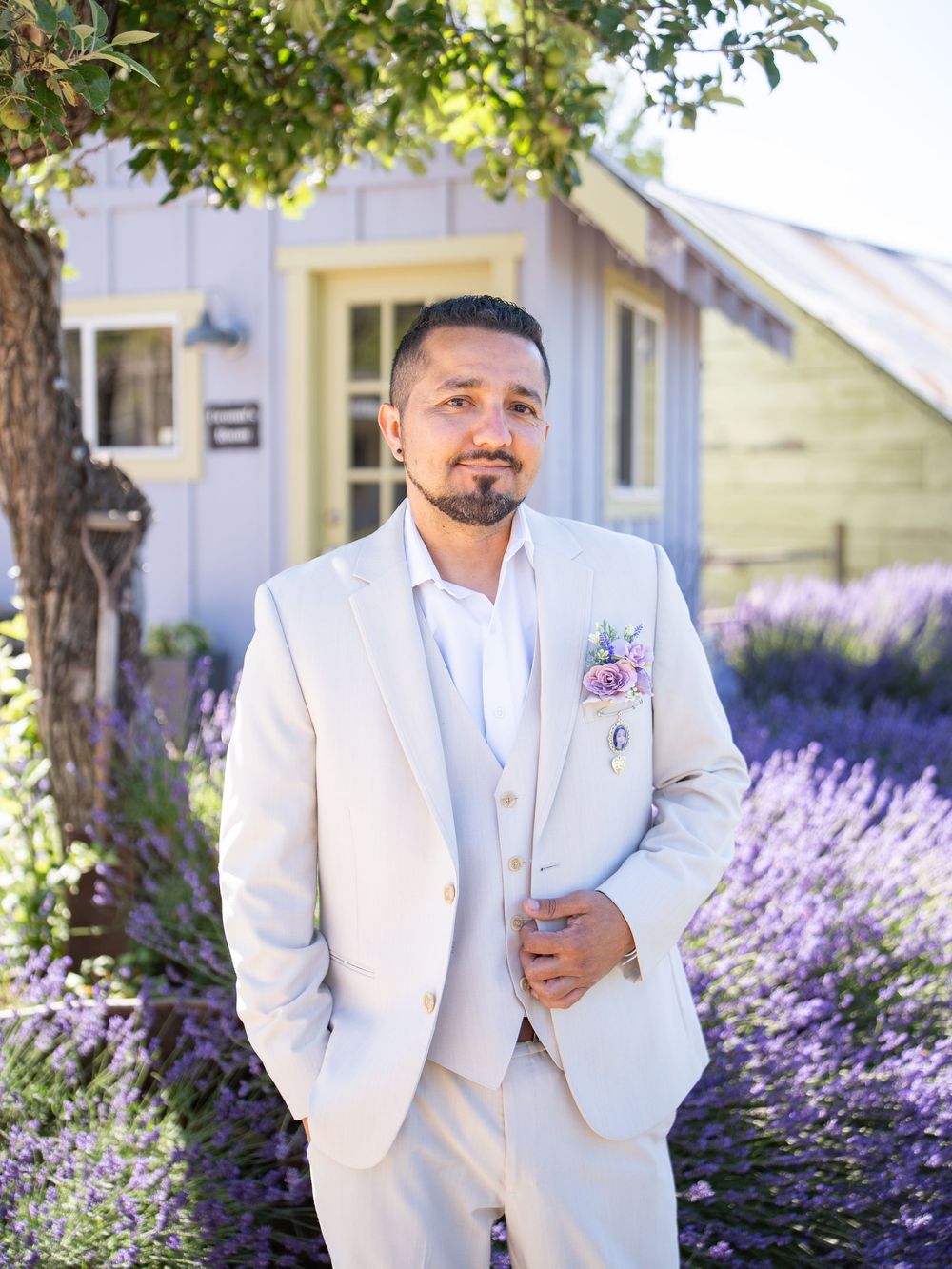 A person in a crisp white suit stands in front of a charming house with blooming lavender bushes in the garden.