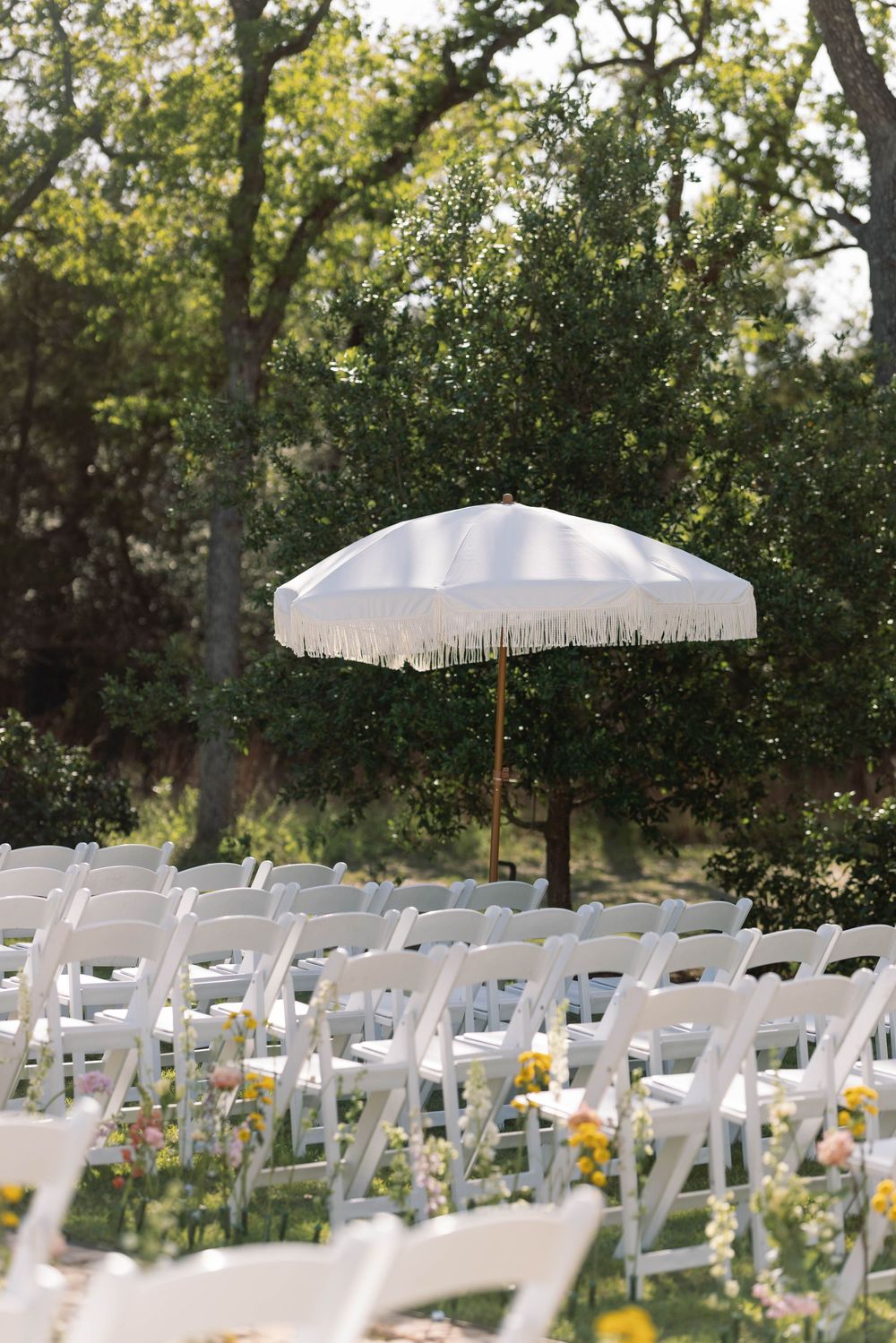 White decorative umbrella stands among rows of folding chairs at an outdoor garden wedding ceremony setup.