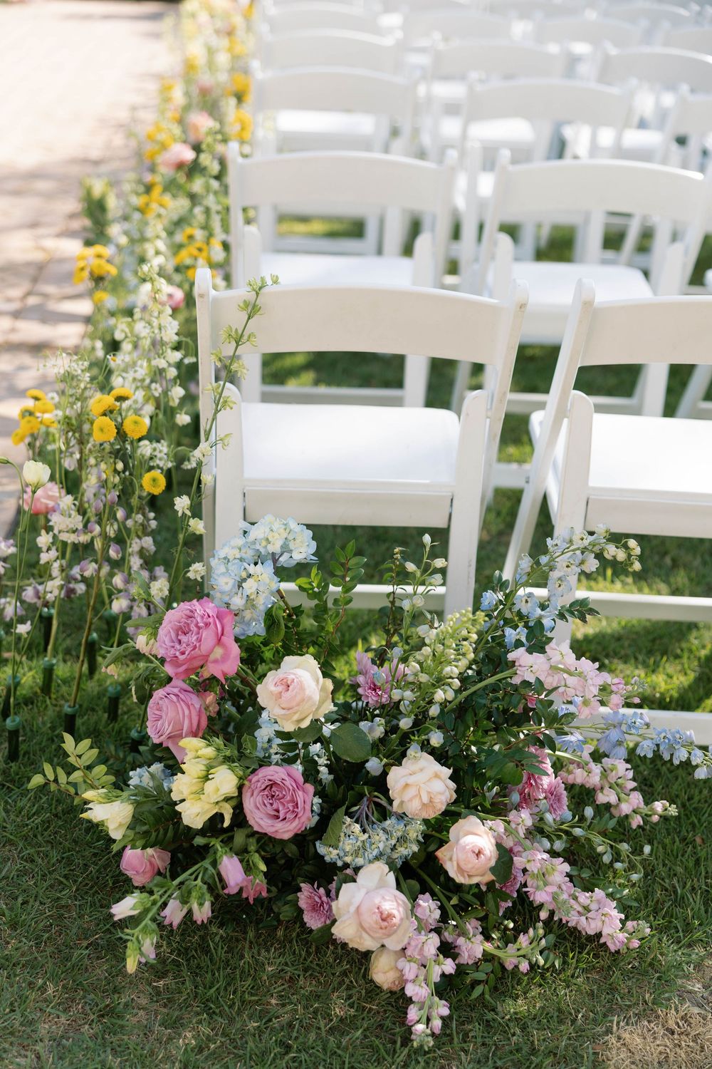 Beautiful floral arrangement with pink and peach roses alongside white garden chairs for an outdoor wedding ceremony.