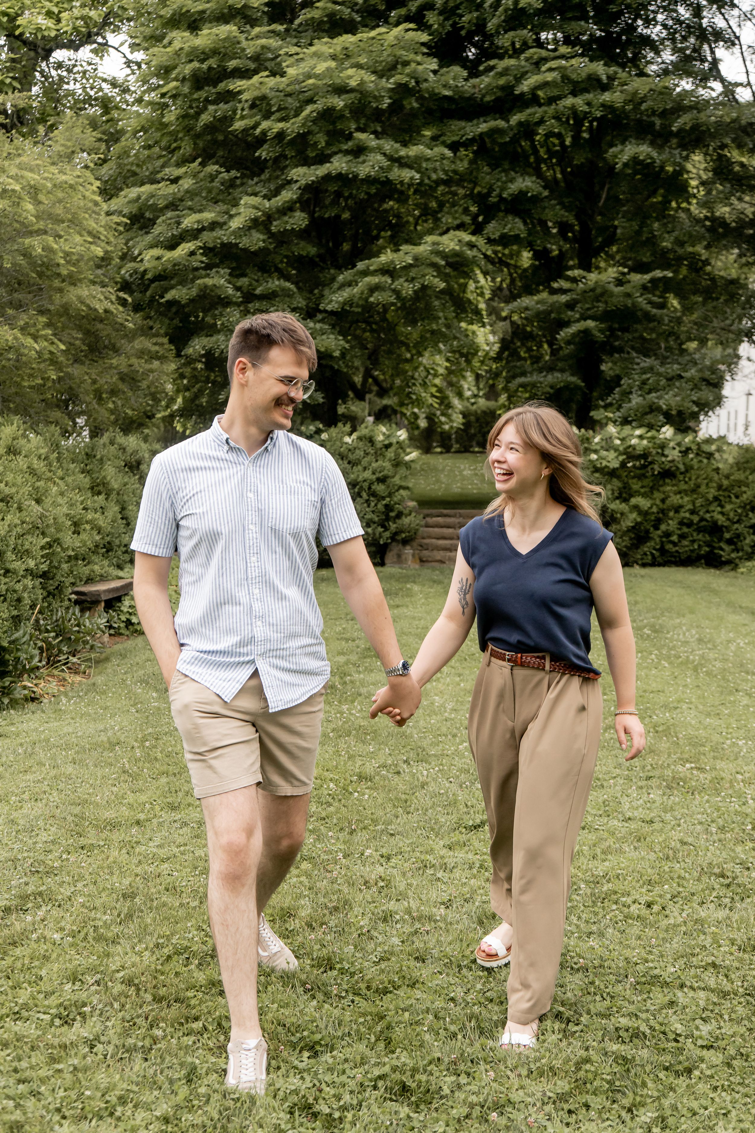 Happy couple holding hands and laughing while walking through a lush green park together.