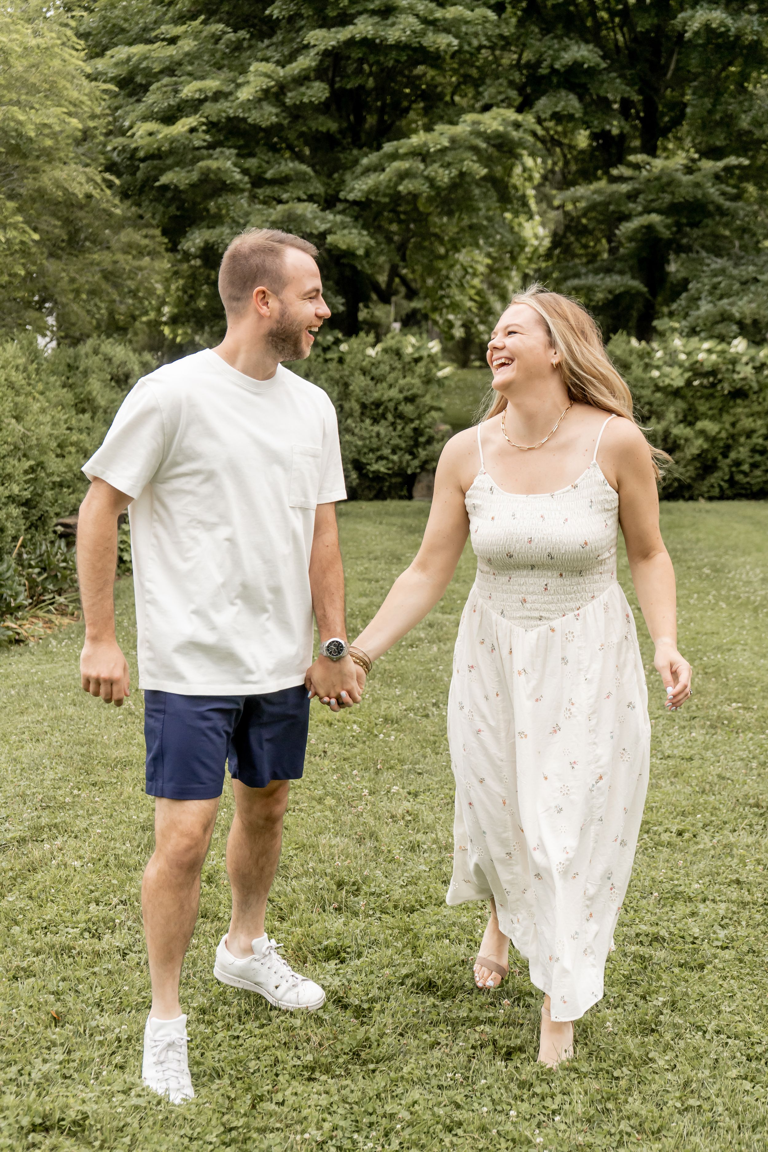 Smiling couple holding hands and walking together through a lush green park on a summer day.