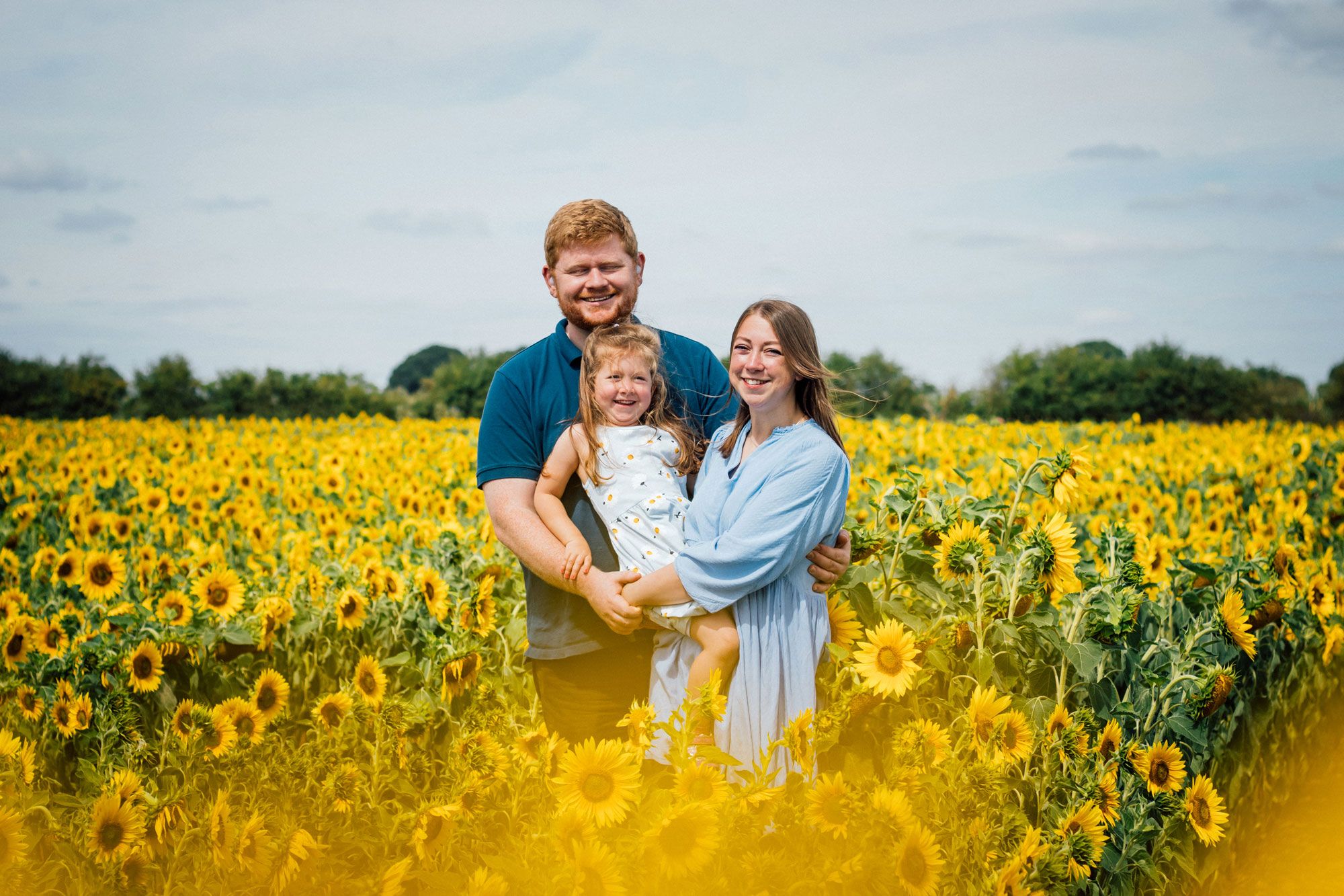 A family poses for a photo surrounded by bright yellow sunflowers in full bloom.