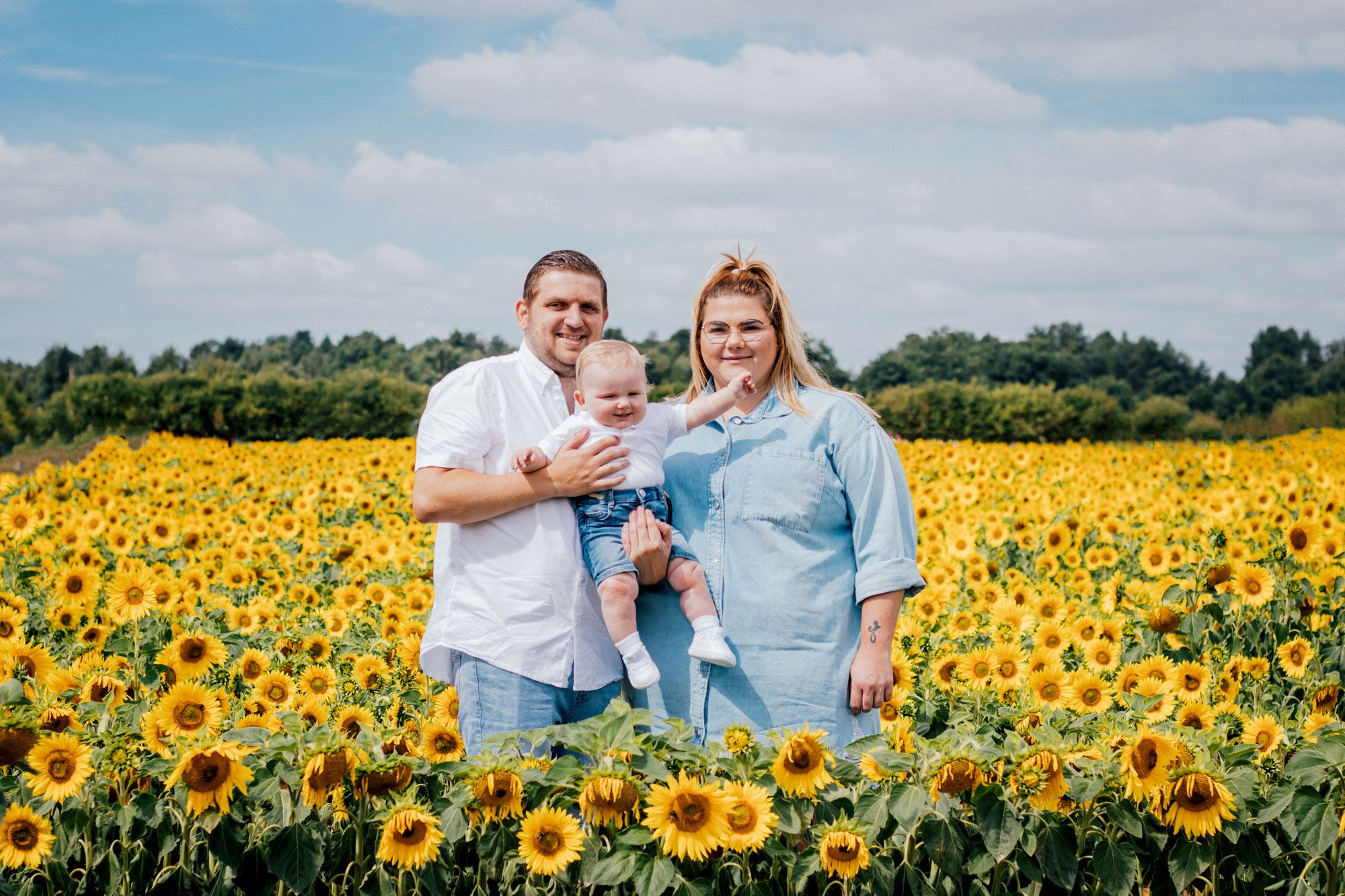A family poses together for a portrait in a bright summer sunflower field on a sunny day.