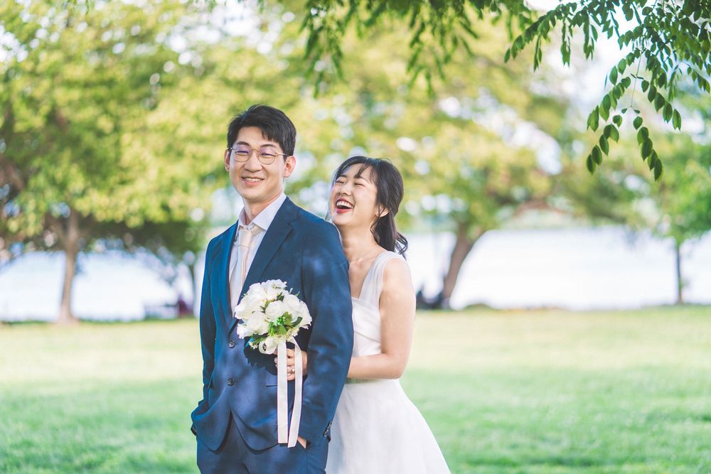 A joyful couple shares a laugh in a sunlit outdoor garden setting with lush greenery in the background.