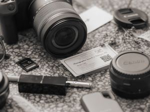 A black and white photograph of camera lenses and photography equipment arranged on a textured surface.