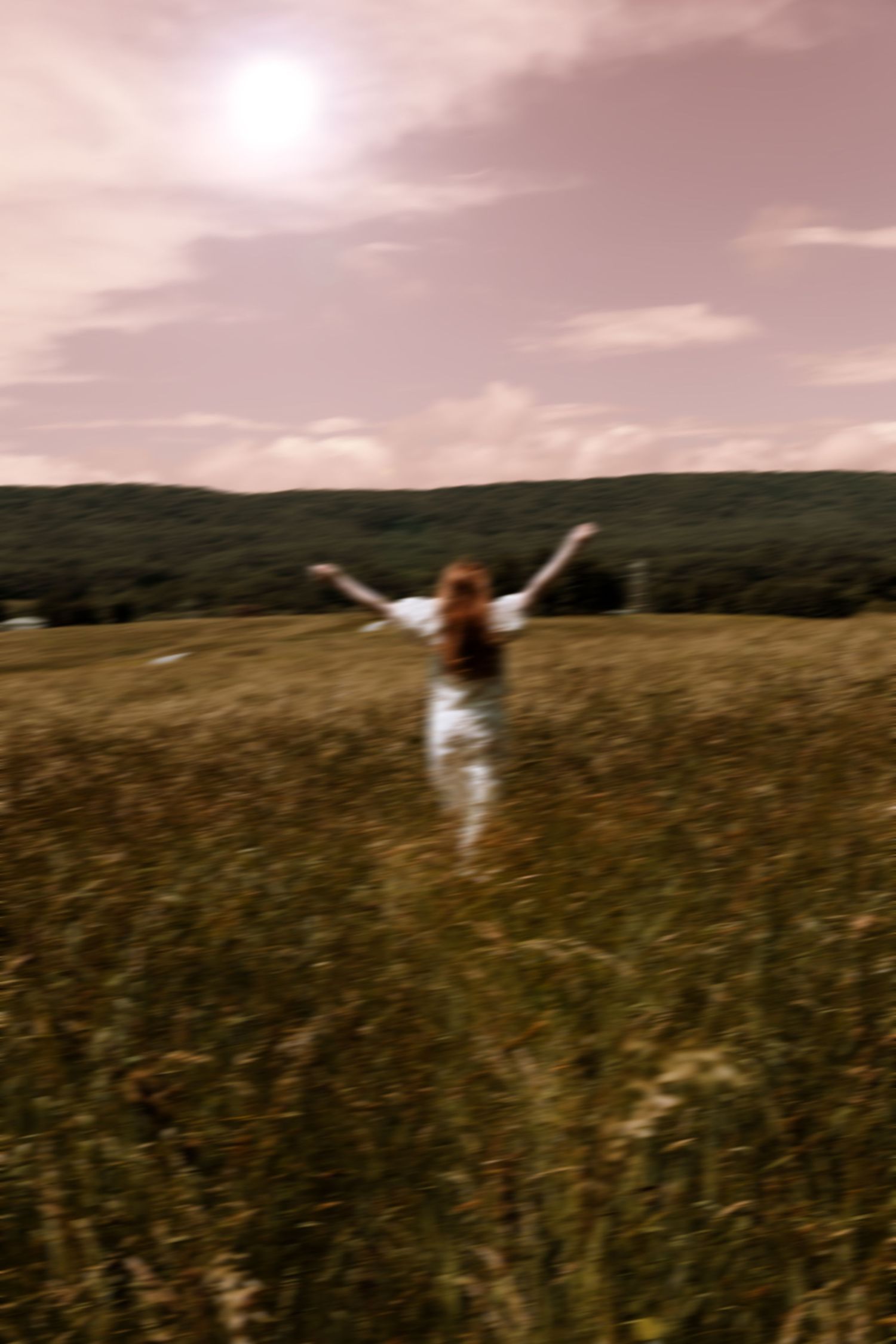 A person in white walks through a vast grassy field at sunset with dramatic clouds overhead, captured in sepia tones.