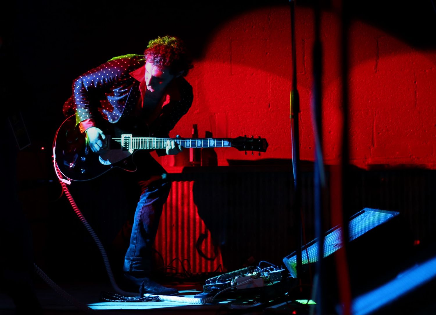 A guitar player is lit by neon light while performing on stage.